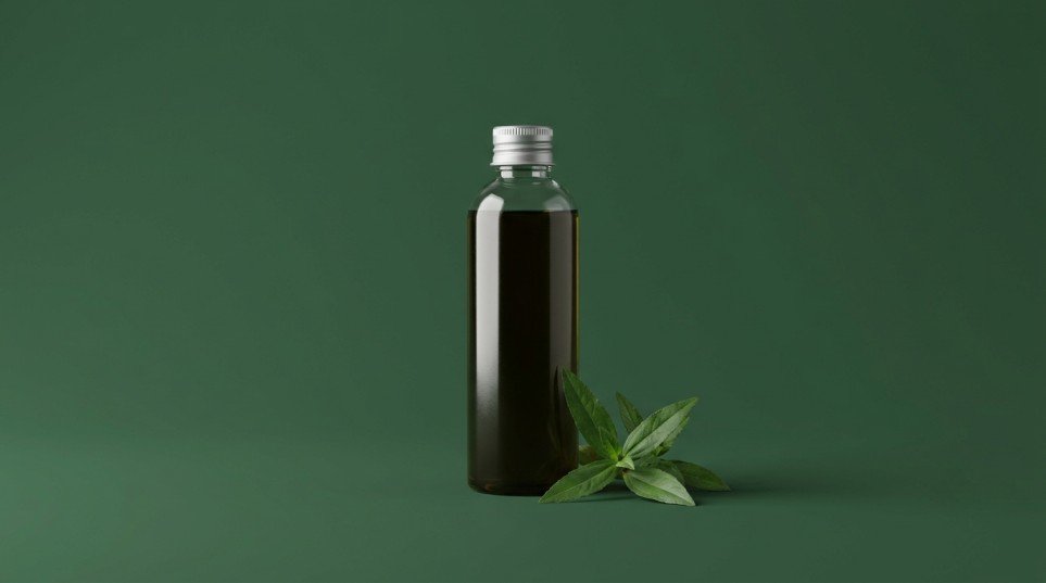 Unbranded glass bottle of bhringraj hair oil with fresh bhringraj leaves on a forest green background